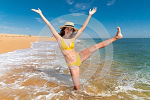 Happy cheerful caucasian woman in a yellow swimsuit and a straw hat dancing fun childishly in the water on the sea on a photo