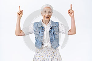 Happy, cheerful charming grandmother, senior lady smiling and laughing carefree, raising hands, pointing fingers up