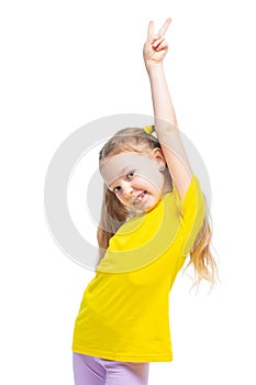 Happy and cheerful child shows victory gesture. The girl is wearing a yellow t-shirt and purple pants.