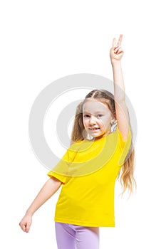 Happy and cheerful child shows victory gesture. The girl is wearing a yellow t-shirt and purple pants.