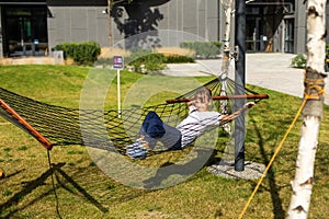 happy cheerful child smiling and lying, resting in a hammock in the woods in a glade in summer among the bright green