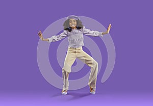 Happy cheerful child in trendy causal outfit dancing on purple studio background