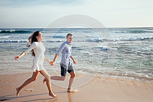 Happy cheerful couple having fun running to the ocean together and doing splashes of water on a tropical beach at sunset
