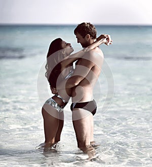 Happy cheerful couple kissing hugging running in the sea together. Romantic vacation, honeymoon love