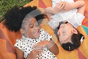 Happy cheerful dark skin girls and caucasian girls laying on mat at outdoors park, Her smiling and laughing together, Relationship