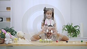 Happy and cheerful daughter is sitting on her father`s shoulders and dancing. Father is sitting under the wooden table