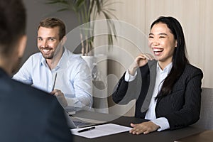 Happy cheerful diverse young colleagues laughing at meeting table