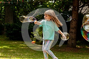 Happy cheerful elementary school age child, girl playing with soap bubbles alone outdoors, summer, one person bubble popping