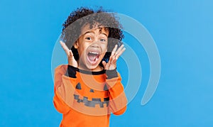 Happy cheerful ethnic boy in a pumpkin costume screams in fright while celebrates Halloween on blue background