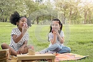 Happy cheerful ethnic girls eat apple together at outdoors park , Relationship little kids, Diverse ethnic concept