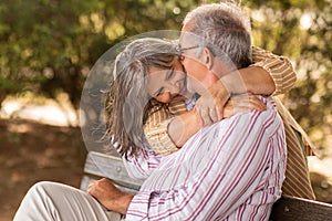 Happy cheerful european mature couple on bench hugging, enjoy date together in park at summer