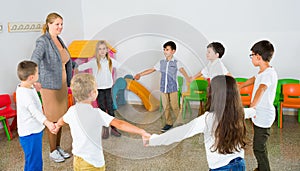 Positive female teacher playing circle game with children in classrom