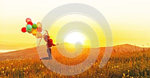 Happy cheerful girl with balloons running across meadow at sunset in summer