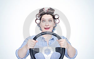 Happy cheerful girl in curlers with steering wheel. Front view. Housewife driving a car.