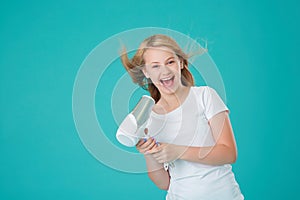 A happy cheerful girl dries her hair with a hair dryer and sings using the hair dryer as a microphone. Blue mint background,