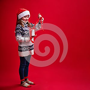 Happy cheerful girl in sweater and Santa's hat opens gift on red background