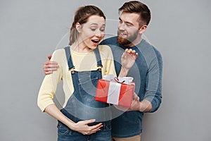 Happy cheerful husband giving present box to his pregnant wife