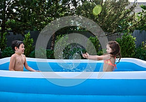 Happy cheerful kids splashing water while playing in the inflatable swimming pool on a beautiful warm sunny summer day