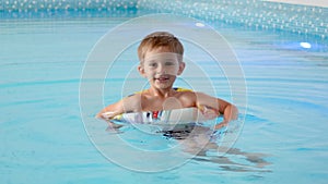 Happy cheerful little boy using inflatable ring while learning swimming in indoor swimming pool at hotel.