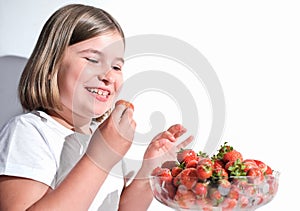 happy cheerful little girl holding fresh strawberrt and going to eat it. schoolgirl with bowl full of strawberries