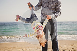 Happy cheerful loving family, father and little daughter playing on beach, young father is holding his kid upside down