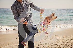 Happy cheerful loving family, father and little daughter playing on beach, young father is holding his kid upside down