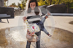 Happy cheerful loving family, mother and little daughter playing in park next to fountain, young mother is holding small girl