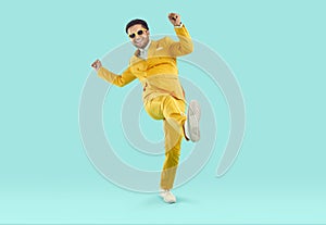 Happy, cheerful man in a yellow suit and sunglasses dancing on a blue studio background