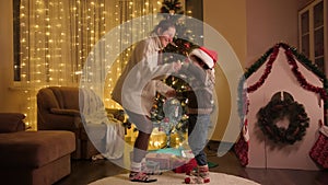 Happy cheerful mother with son dancing and having fun next to Christmas tree in living room. Pure emotions of families