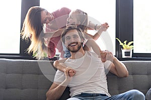 Happy cheerful parents having fun with cute children daughters playing on sofa