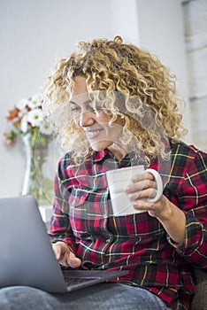 Happy cheerful pretty young woman with blonde curly hair work and smile with laptop computer sit down on the sofa at home -