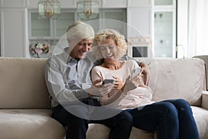 Happy cheerful retired couple using online apps on smartphones