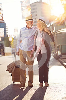 Happy cheerful senior couple of tourists with map and city guide walking on street