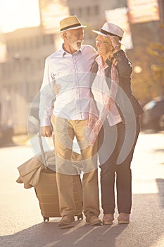 Happy cheerful senior couple of tourists with map and city guide walking on street