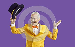 Happy cheerful senior man in yellow suit greets you and takes off his black top hat