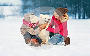 Happy cheerful smiling family playing having fun together in winter day, mother and child walking with white Samoyed dog in snowy