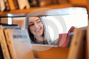 Happy cheerful student girl among books in library