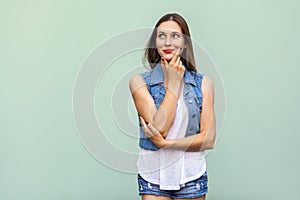 Happy cheerful teenage girl with freckles, casual style white t shirt and jeans jacket, looking up, thinking and touching her face