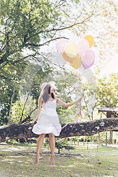 Happy cheerful woman holding colorful of balloons wear sunglasses on green meadow with cloudy blue sky.