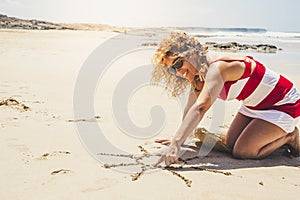 Happy cheerful woman on summer holiday vacation enjoying the beach and the outdoor designing a sun on the sand - beautiful curly