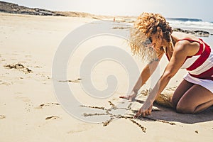 Happy cheerful woman on summer vacation enjoying the beach and the outdoor designing a sun on the sand - beautiful curly caucasian