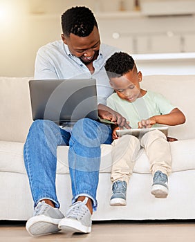 Happy cheerful young african american man using a laptop while helping his son with a digital tablet sitting on the