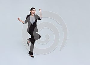 Happy cheerful young Asian businesswoman in suit jumping in mid-air isolated on studio white background