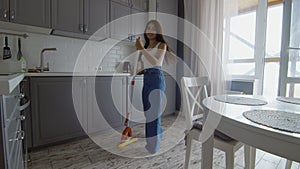 Happy and Cheerful young beautiful woman cleans floor and dances with mop like with guitar