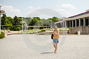 Happy cheerful young blond woman with backpack walking on city street checks her smartphone. Portrait of beautiful 30s