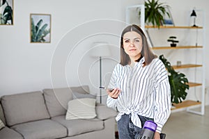 Happy cheerful young Caucasian beautiful woman vacuuming floor and using smartphone at home in living room, domestic concept