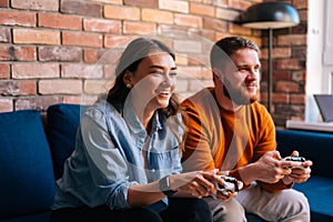 Happy cheerful young couple holding controllers and playing video games on console sitting together on couch