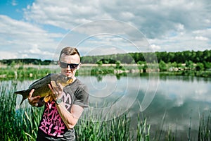 Happy cheerful young fisherman hold a big fish carp on a background of lake and nature. Fishing background. Good catch. Trophy