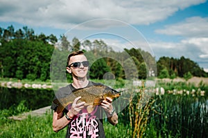 Happy cheerful young fisherman hold a big fish carp on a background of lake and nature. Fishing background. Good catch. Trophy