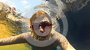 Happy cheerful young woman in blue swimming suite in swimming pool, underwater view. Action camera